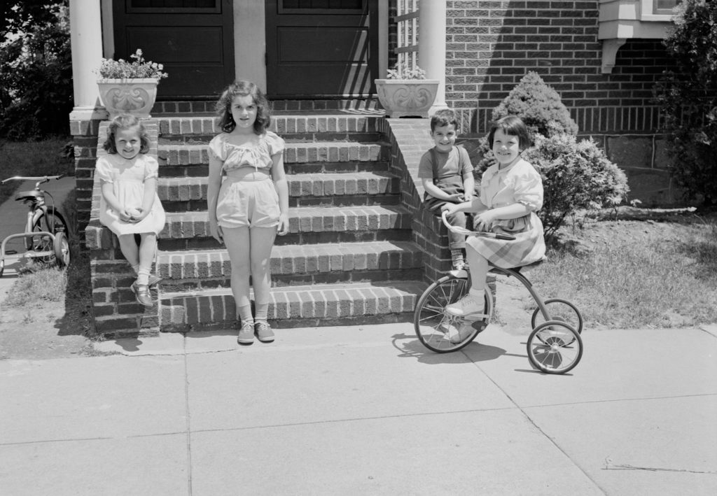 Black and white vintage picture of kids on steps and one on a tricycle.